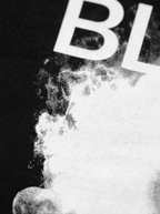BLOW ME tee — extreme close-up of the smoke print texture on black cotton